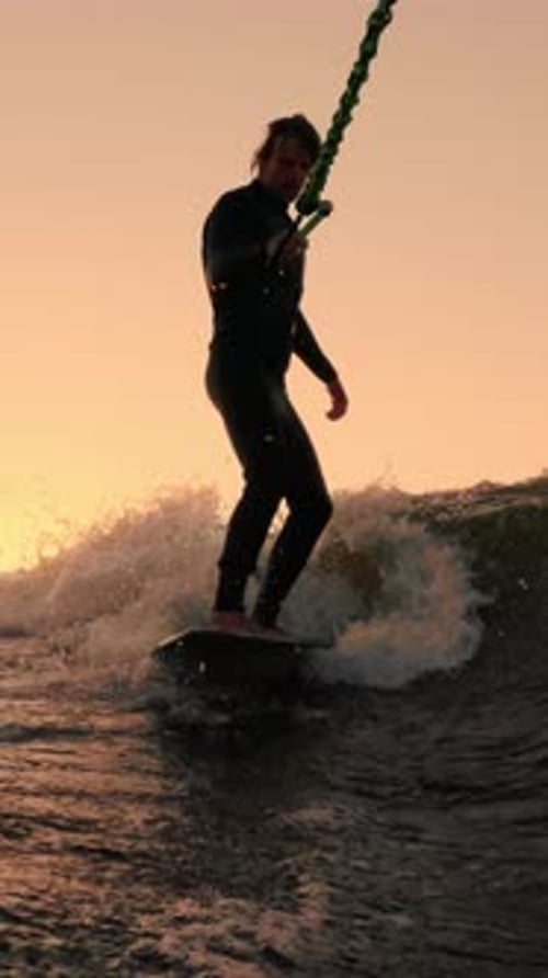 Man Wakeboarding on Water at Sunset in Wetsuit