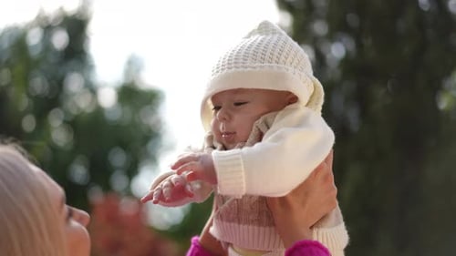 Woman Holds Laughing Baby Outdoors in Daylight