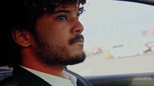 A Curlyhaired Man in a Business Suit is Driving a Car A Young Indian Businessman is Driving to a