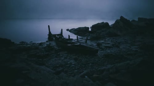 Forgotten Boat Rests on a Rocky Shore Under the Twilight Sky