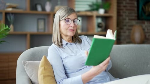Mature Woman Reading a Book on Couch at Home
