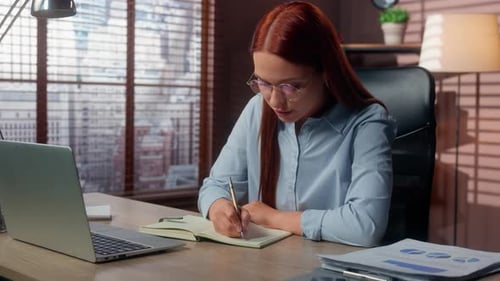 Concentrated Caucasian Business Woman Working Laptop in Office Writing Notes in Notebook Handwriting