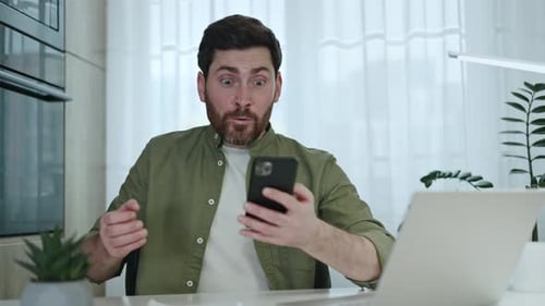 Man Celebrates with Smartphone at Home