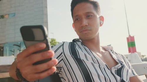 Young man tourist sits on bench on the pier and uses mobile phone