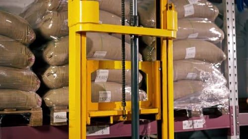 Close Up A Worker at Coffee Factory Uses a Yellow Lifting Fork to Lift and Insert Forks Into Pallets