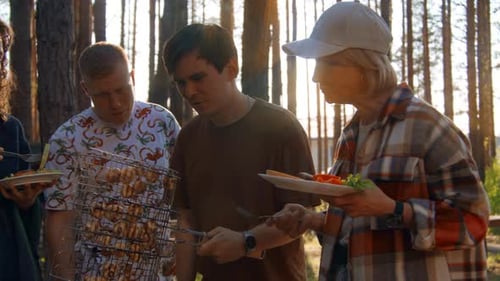 Friends have fun relaxing in nature and eat delicious food on grill
