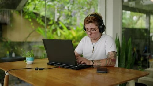 Transgender Musician Composes Music on Laptop at Coffee Shop Freelancer in Headphones Creates