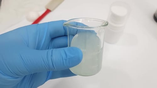 Plan rapproché d'un bécher de laboratoire rempli d'un liquide trouble. Une main gantée tient le bécher c
