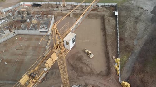 Zumbido vuela de cerca a una grúa alta amarilla con una obra en construcción al fondo, una excavadora y una obra