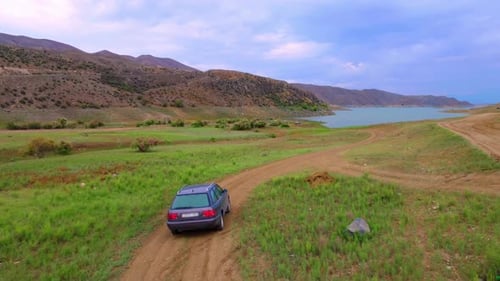 drone of car moving along road to lake among rural roads and mountains