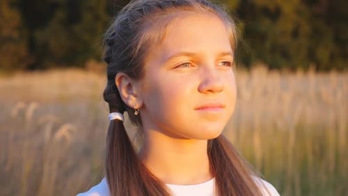 Portrait of Happy Little Girl Stands at Grass Meadow Looking at Beautiful Evening Sunset Cute Female
