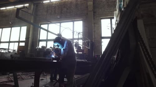 Arbeiter schweißt ein Metallstück mit Funkenflug auf einem großen Stahlwerk. Industrieller Prozess