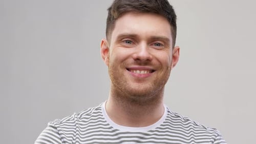 Glücklicher junger Mann im gestreiften T-Shirt, der auf grauem Hintergrund lächelt