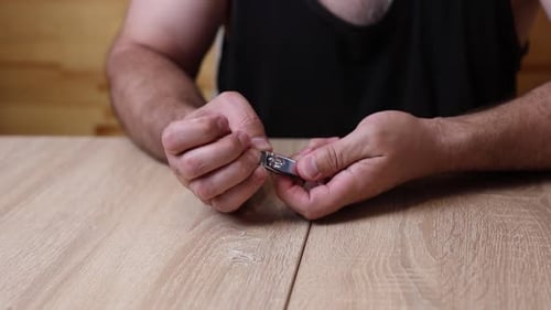 Man Trims Fingernails With Clippers At Table