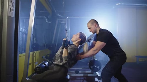 The Trainer Shows How to Correctly Perform Exercises on the Simulator in the Gym