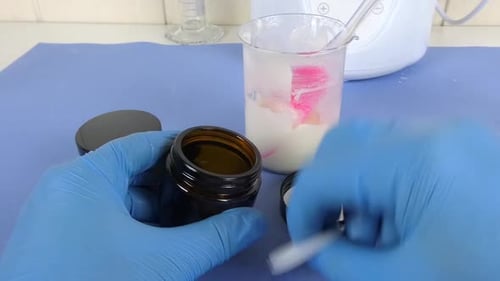 vue d'une scène de laboratoire de cosmétiques où un opérateur ganté utilise une spatule pour emballer soigneusement un sachet