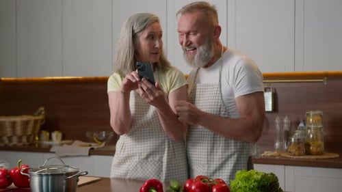 Smiling Seniors Using Smartphone in Kitchen