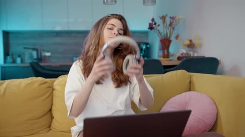 Woman Puts On Headphones and Works on Laptop