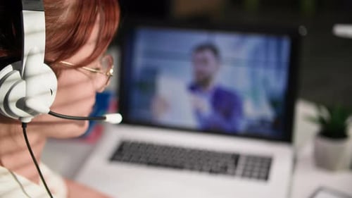 Online Conference Young Female Employee with a Headset Communicates with Boss Via Video Link on a