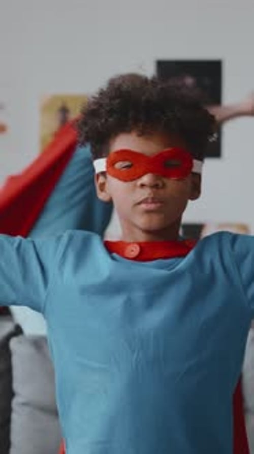 Little African American Boy in Superhero Cape and Mask Showing Biceps on Camera