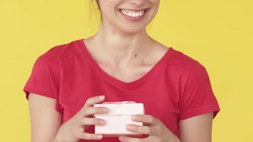 Woman Opens Small Gift on Yellow Background