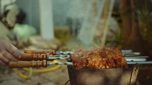 A man's hand flips kebab on skewers on the veranda on a summer day warm summer tones video