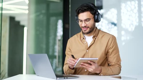 Young Adult with Laptop Writing in Notebook