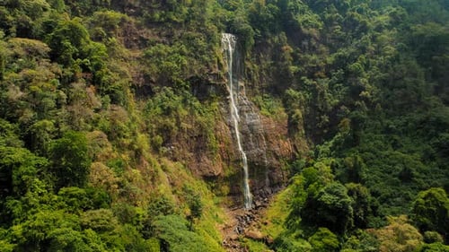 Tall rainforest waterfall cascading down a cliffside, distant aerial view