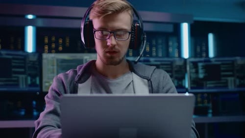 Man Coding on Laptop in Data Center at Night