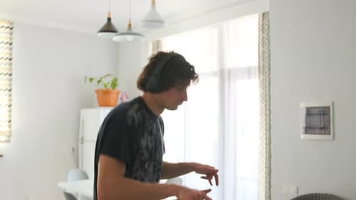 Primer plano de un joven bailando rítmicamente con auriculares inalámbricos en casa