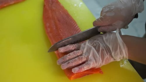 A man's hand in a white glove cuts a portion of fresh sea salmon, red fish fillet on a cutting board