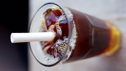 Cold brew coffee and bubble tea in a glass with ice and big white straw close up slow motion, vertic