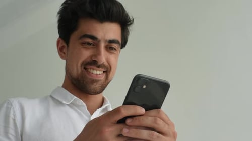 Closeup Lowangle View Face of Cheerful Bearded Young Man Holding Smartphone Using Mobile Apps Having