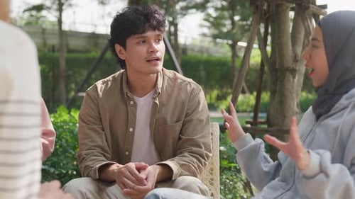 Small Asian group of people sit in a close circle and talk to a therapist in park.