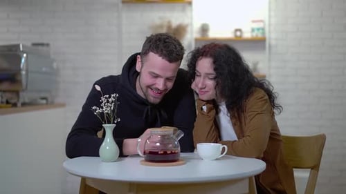 Medium Shot Joyful Young Couple Scrolling Smartphone App Talking Enjoying Leisure in Cafe Portrait