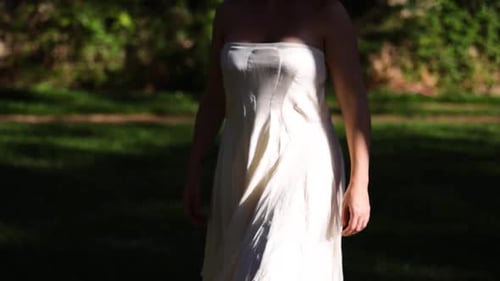 woman with a white strapless summer dress walk slowly outdoors from the shadow into the sun opening