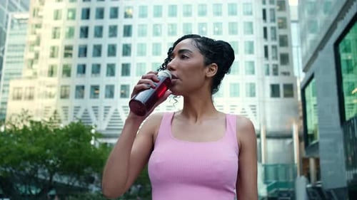 Retrato de una joven mujer en forma bebiendo una bebida energética de una botella.
