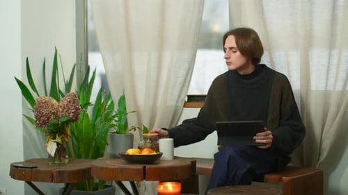 Young Man is Sitting in Cafe with Tea and Tablet Media Man in Cozy Cafe is Working on Tablet and