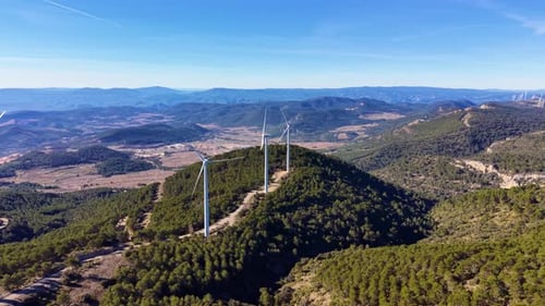 Still wind turbines on a forested mountain ridge with sweeping valley and mountain range views