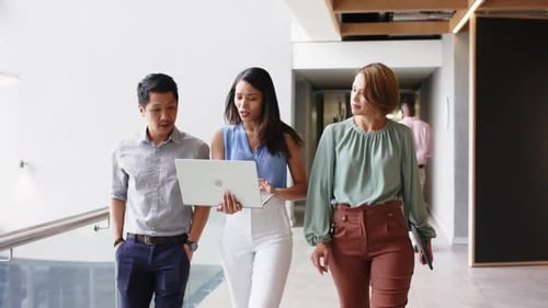Walking in office, business colleagues discussing work while using laptop