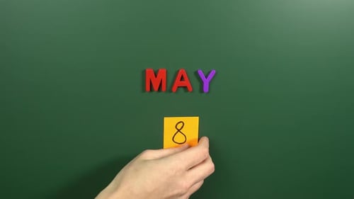 Hand sticking a sticker 8 May calendar day on school board. 8 date of May. Eighth day May. 8th