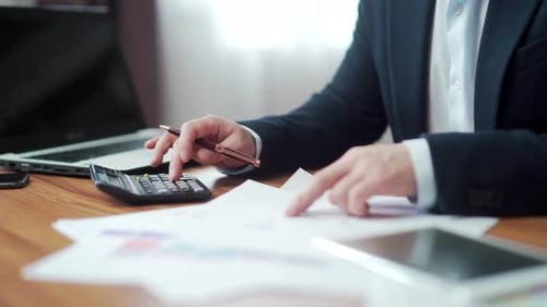 hands close up of financial analyst accountant at desk counting report on calculator with documents