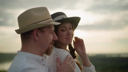 Lovers Embracing at Sunset Both Wearing White Shirts and Hats