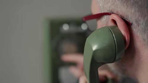 Closeup of a Man in Glasses Dialing a Number on a Vintage Rotary Telephone The Scene Represents