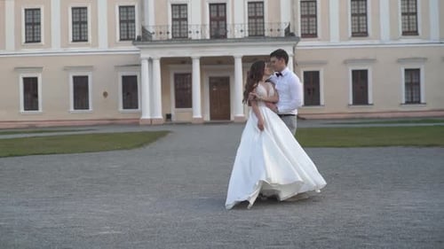 Happy wedding couple spinning together at sunset on the background of a beautiful building