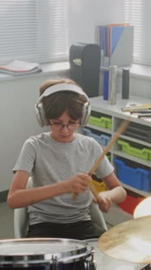 Primary School Boy Wearing Headphones Practicing Drums in Modern Music Class
