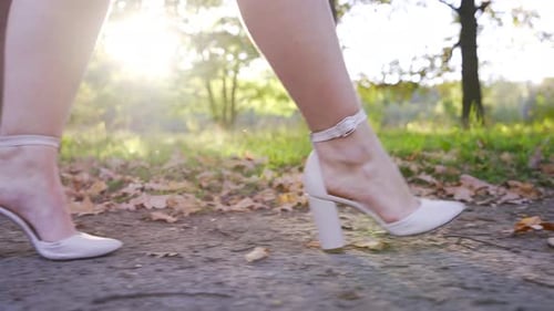 Unrecognizable Woman Legs in High Heels Walks Through City Park in Autumn in Sunset Light