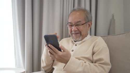 Senior Man Uses Smartphone Indoors on Couch