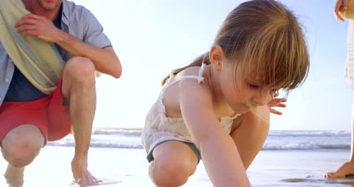 4k video footage of a little girl drawing in the sand at the beach while bonding with her parents