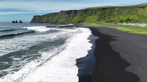 Aerial view of the iconic Víkurfjara black sand beach in Iceland, with powerful ocean waves rolling